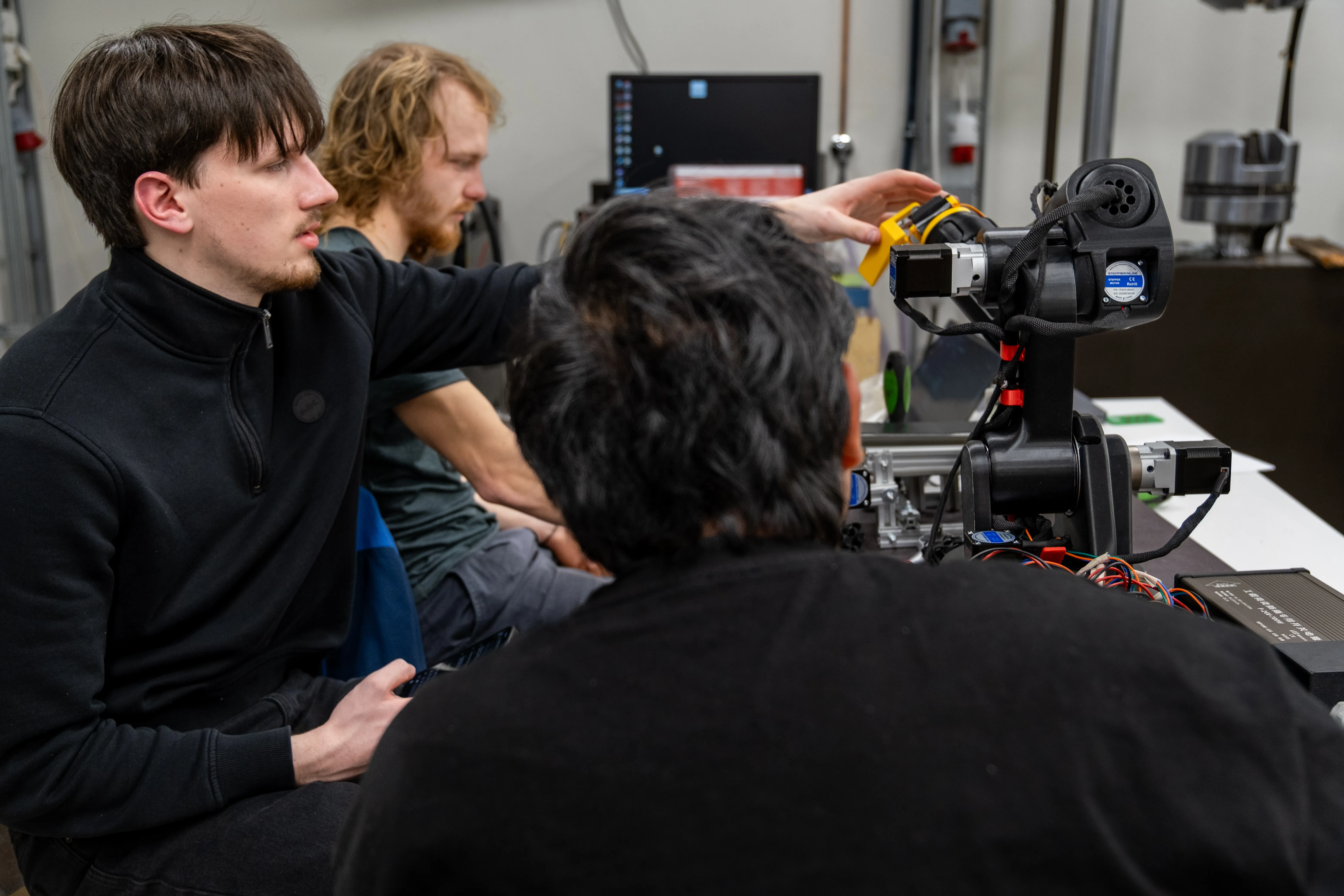 Three students are working with Proto-GK-RA robot. One students is physically fixing robot's end-effector.