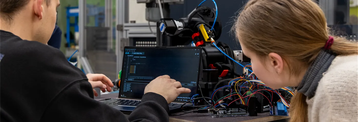 A photo of two students inside the university's laboratory on the background of Proto-GK-RA. One of the students is using a laptop.